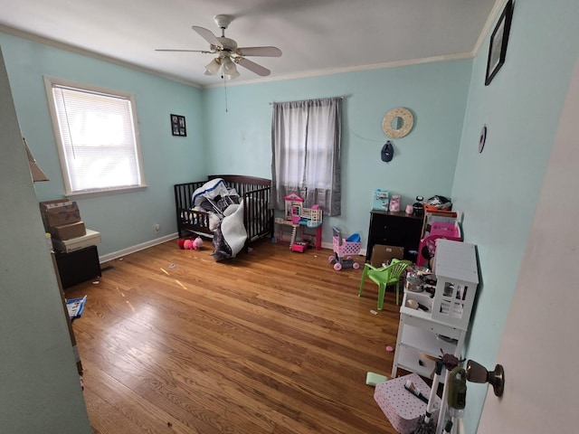 bedroom featuring a nursery area, wood finished floors, baseboards, and ornamental molding