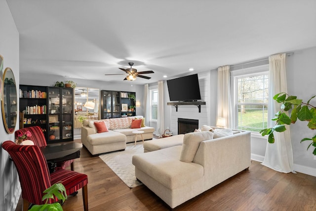 living room with a ceiling fan, baseboards, recessed lighting, dark wood-type flooring, and a large fireplace