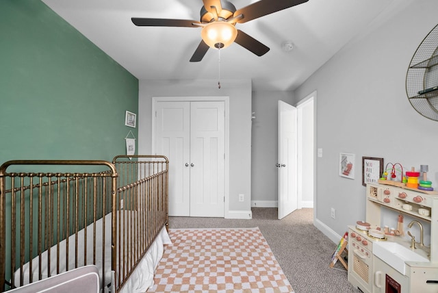 bedroom with baseboards, carpet floors, ceiling fan, a crib, and a closet