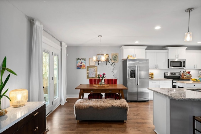 kitchen featuring light stone counters, dark wood-style floors, stainless steel appliances, decorative backsplash, and white cabinets