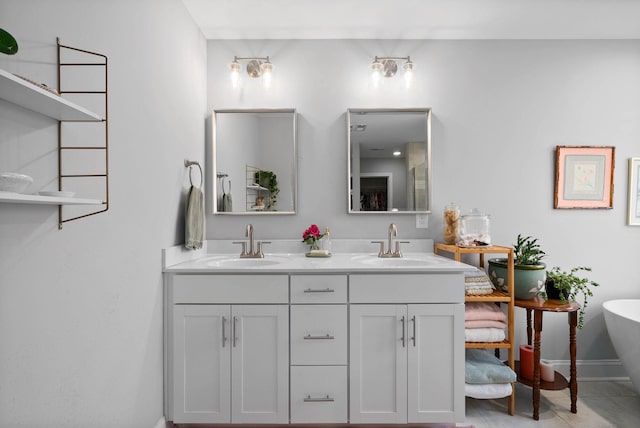 full bath with double vanity, a freestanding bath, baseboards, and a sink