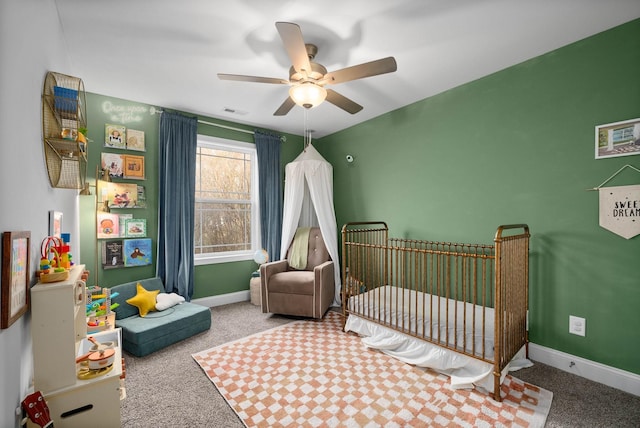 bedroom with visible vents, a crib, baseboards, carpet flooring, and a ceiling fan