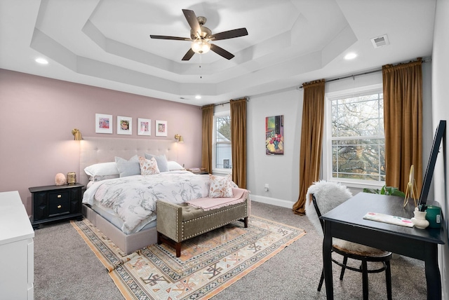 bedroom featuring a tray ceiling, multiple windows, visible vents, and light carpet