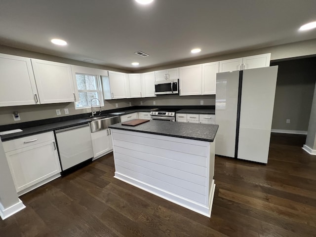 kitchen featuring dark wood finished floors, a sink, appliances with stainless steel finishes, white cabinetry, and dark countertops