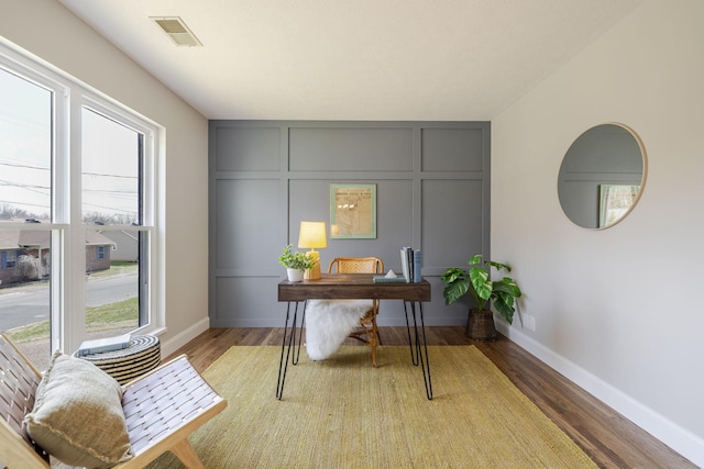 office area featuring visible vents, baseboards, light wood-style floors, and a decorative wall