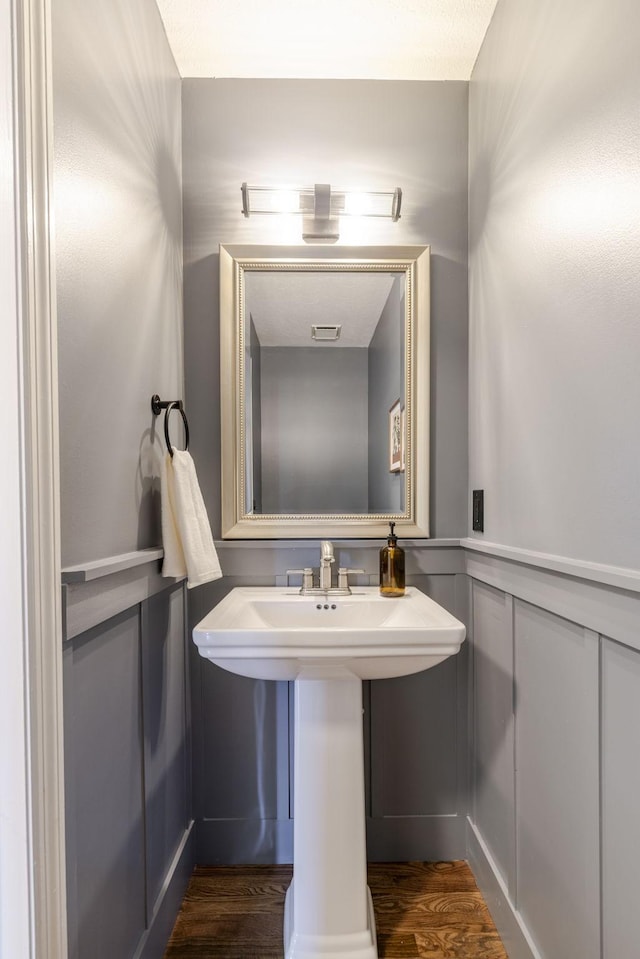 bathroom with visible vents, wainscoting, wood finished floors, a decorative wall, and a sink