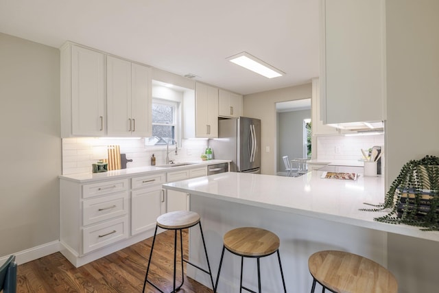 kitchen with dark wood finished floors, a peninsula, freestanding refrigerator, white cabinetry, and a sink