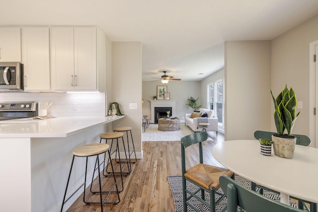 kitchen featuring stainless steel microwave, a breakfast bar area, white cabinetry, and decorative backsplash