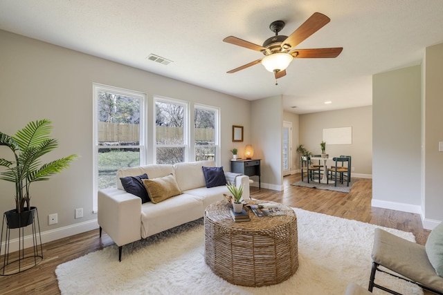 living area featuring visible vents, baseboards, ceiling fan, and wood finished floors