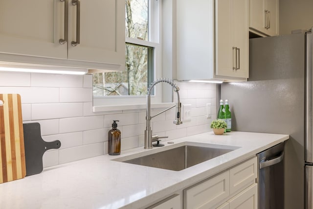 kitchen featuring a sink, light stone countertops, decorative backsplash, white cabinets, and stainless steel dishwasher