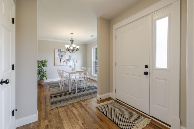 entryway with baseboards, a notable chandelier, wood finished floors, and ornamental molding