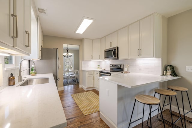 kitchen with visible vents, a sink, appliances with stainless steel finishes, a peninsula, and light countertops