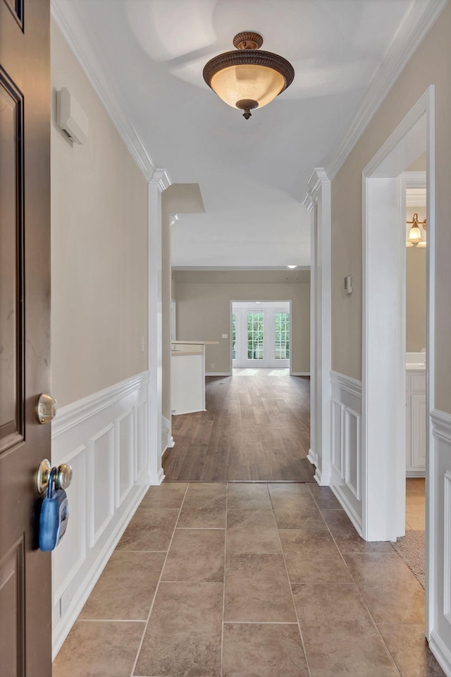 hall with tile patterned floors, a wainscoted wall, crown molding, and a decorative wall