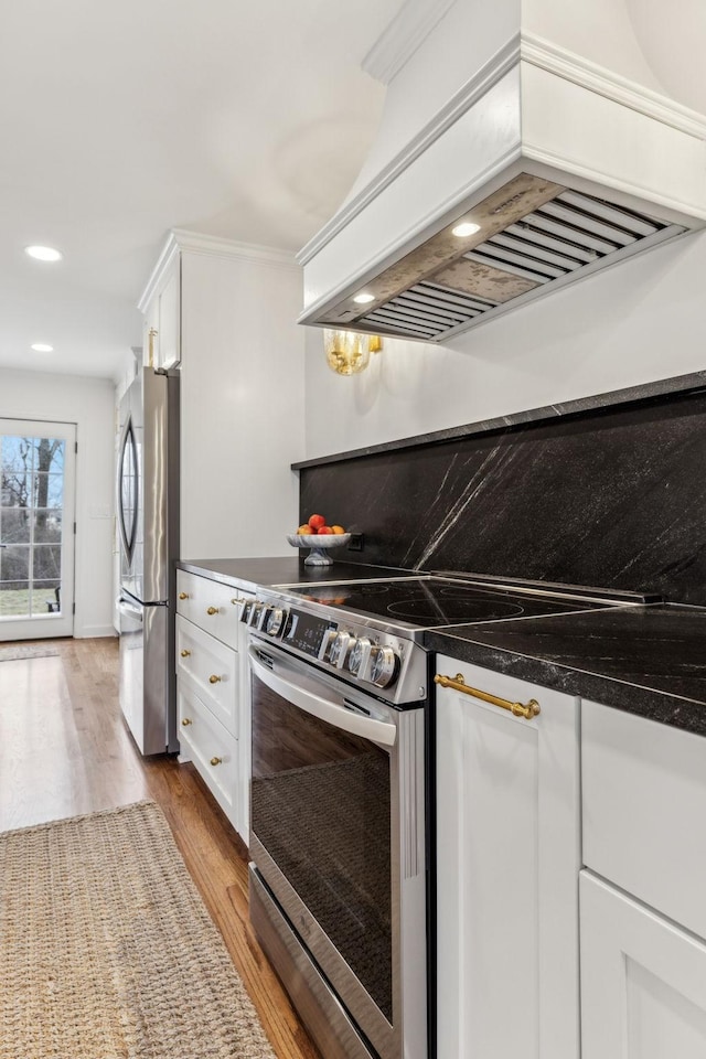 kitchen with custom exhaust hood, white cabinets, light wood-style floors, and appliances with stainless steel finishes