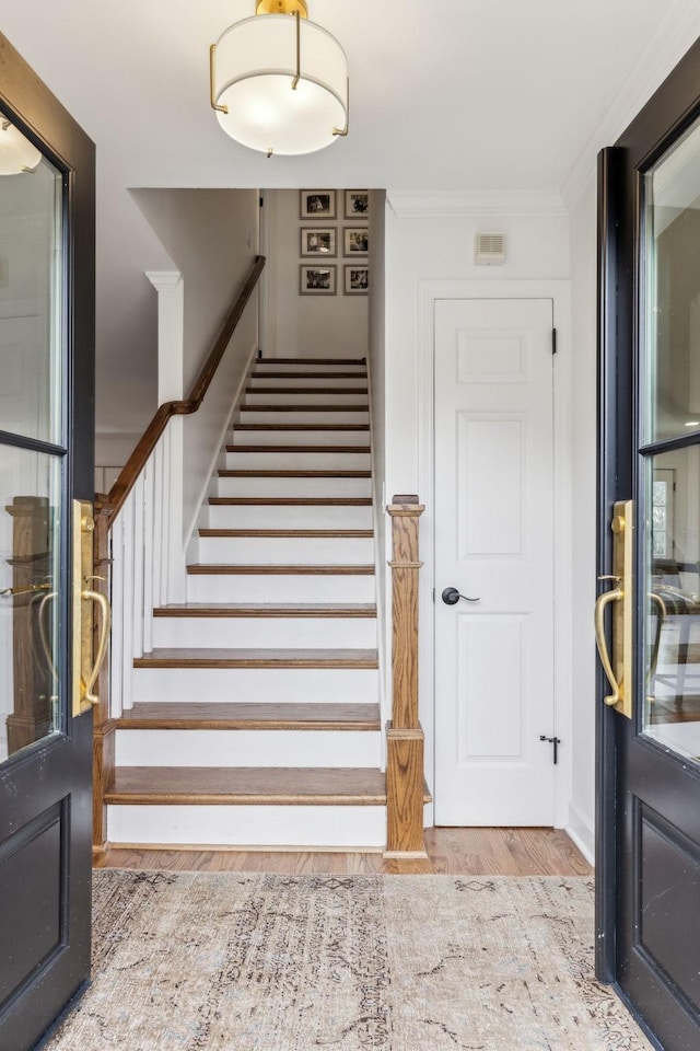 stairway with wood finished floors and ornamental molding