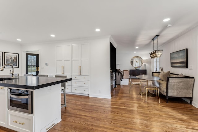 kitchen with dark countertops, a sink, white cabinets, light wood-style floors, and stainless steel oven