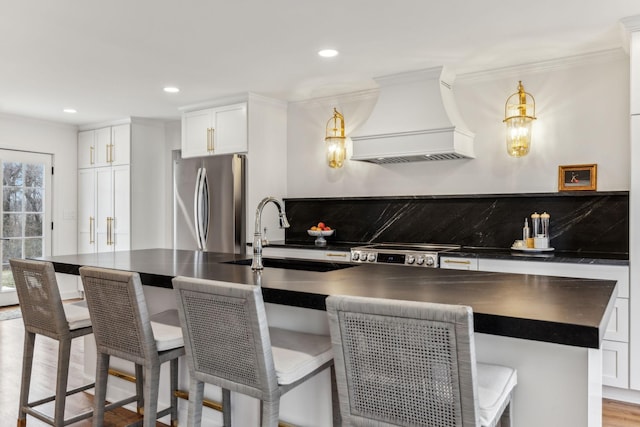 kitchen featuring dark countertops, backsplash, premium range hood, freestanding refrigerator, and a sink