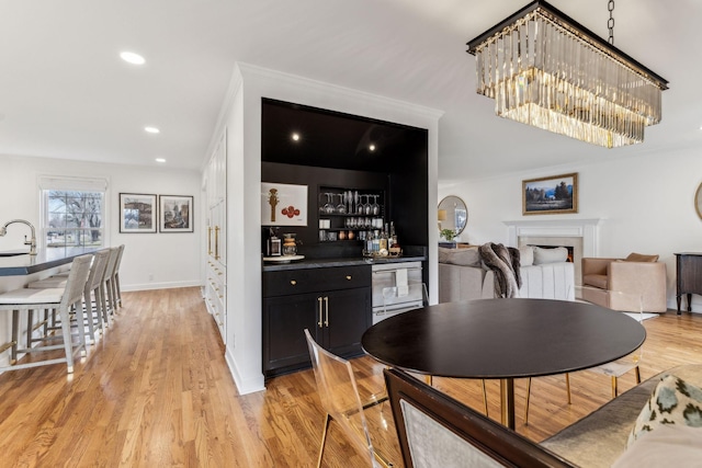 dining space featuring light wood-type flooring, recessed lighting, a bar, a fireplace, and baseboards