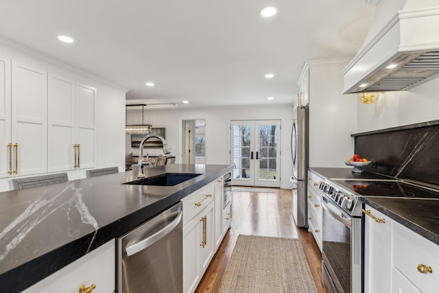 kitchen with a sink, stainless steel appliances, custom range hood, french doors, and white cabinetry