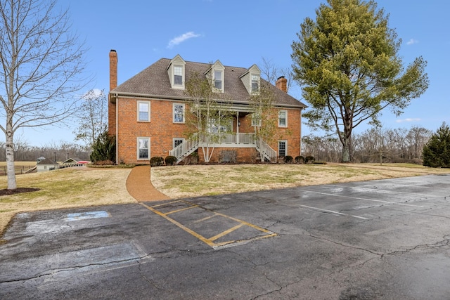 view of front of property with a porch, uncovered parking, a front yard, brick siding, and a chimney