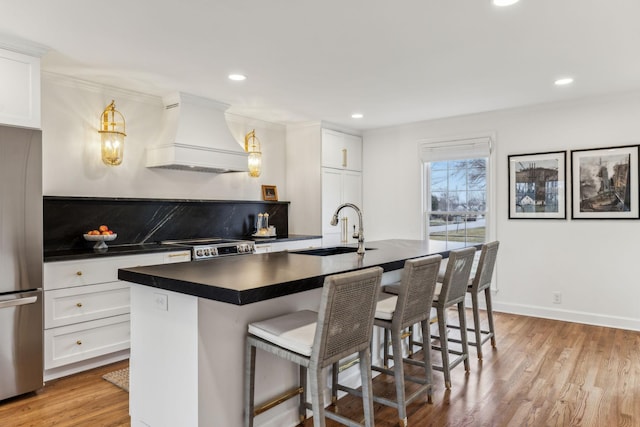 kitchen with a sink, dark countertops, stainless steel appliances, light wood-style floors, and custom exhaust hood