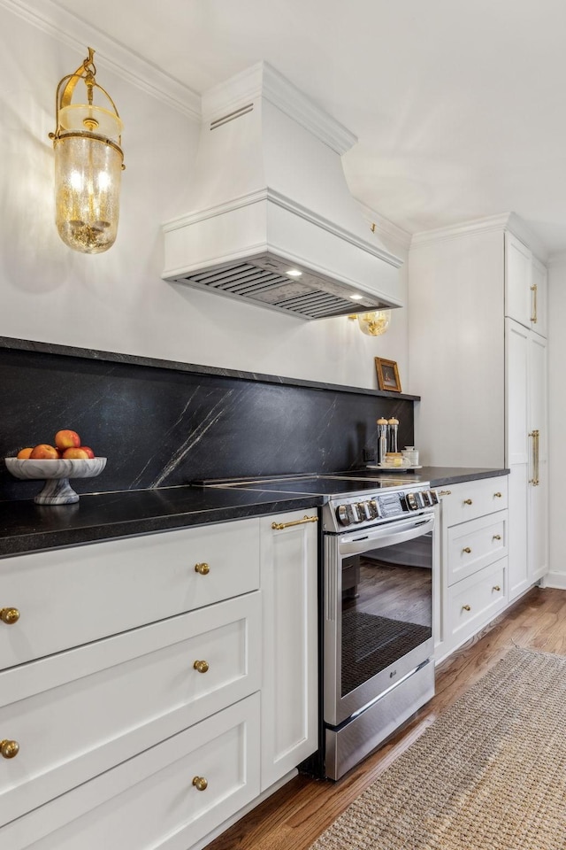 kitchen featuring dark countertops, premium range hood, ornamental molding, wood finished floors, and white cabinetry