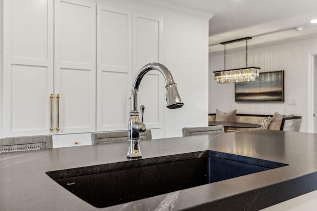 room details featuring a sink, dark countertops, white cabinets, a chandelier, and hanging light fixtures