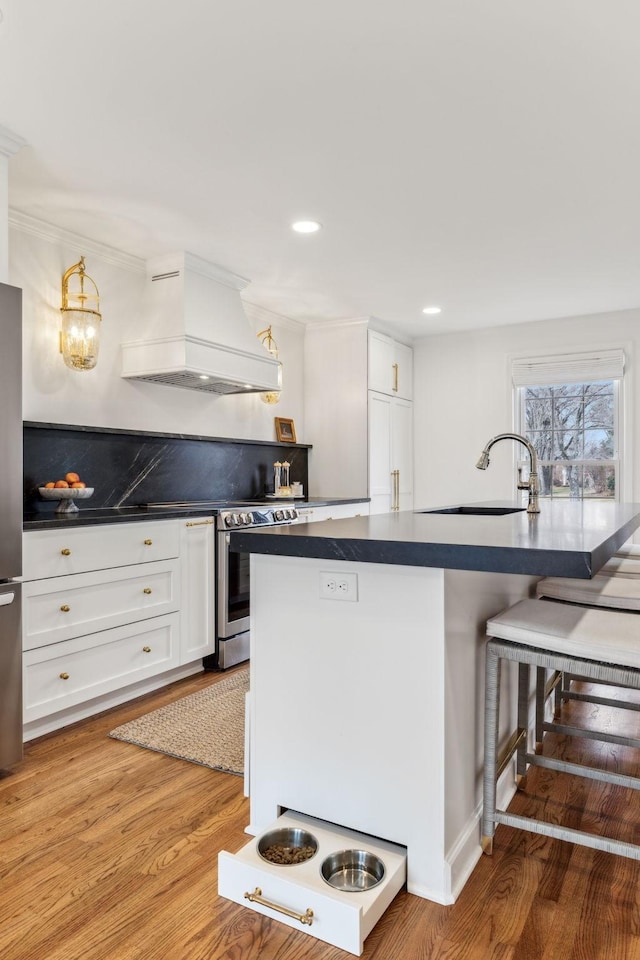 kitchen with custom exhaust hood, stainless steel appliances, a sink, a kitchen bar, and dark countertops