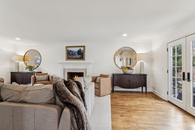 living area with recessed lighting, a lit fireplace, french doors, crown molding, and light wood-type flooring