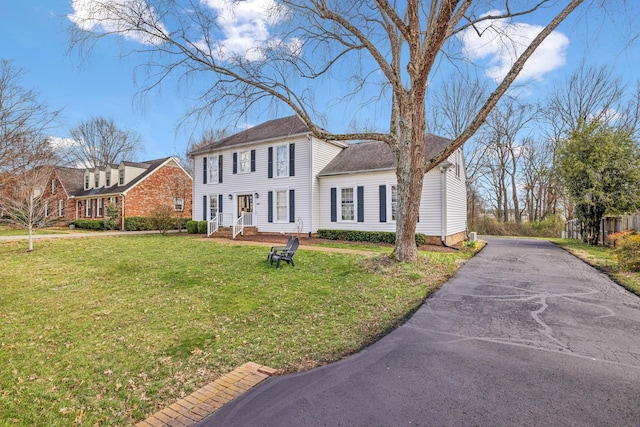 colonial home featuring aphalt driveway, a front yard, and a shingled roof