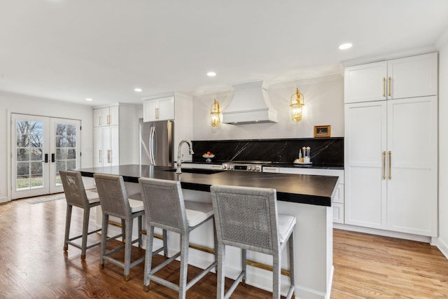 kitchen with dark countertops, custom range hood, light wood-style flooring, freestanding refrigerator, and a sink