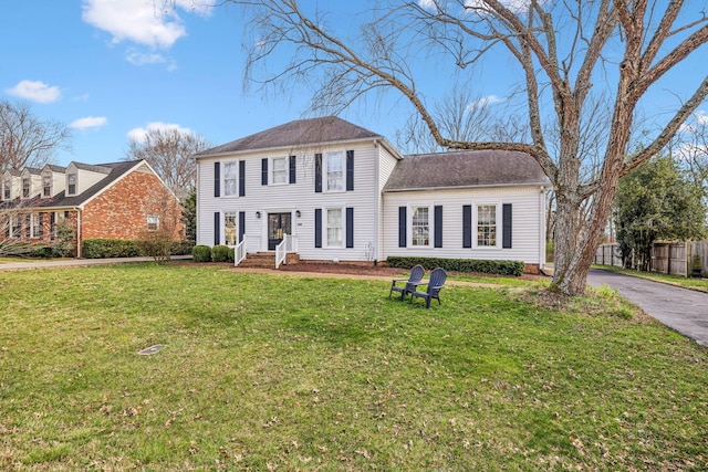 colonial-style house featuring aphalt driveway, a front lawn, and fence