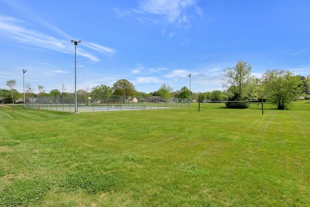 view of community with a tennis court, a yard, and fence