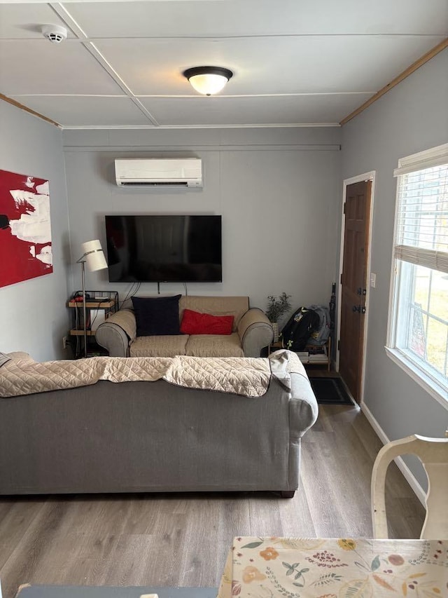 living area featuring ornamental molding, baseboards, a wall unit AC, and wood finished floors