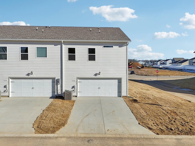 exterior space with central air condition unit, an attached garage, a shingled roof, and concrete driveway