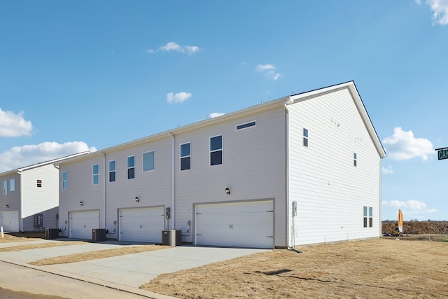 back of property with driveway, central AC, and a garage