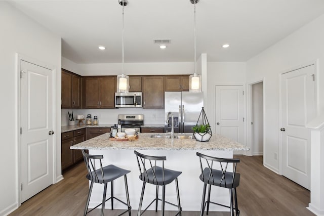 kitchen with a kitchen bar, an island with sink, wood finished floors, and stainless steel appliances
