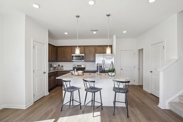kitchen featuring a kitchen bar, wood finished floors, stainless steel appliances, and visible vents
