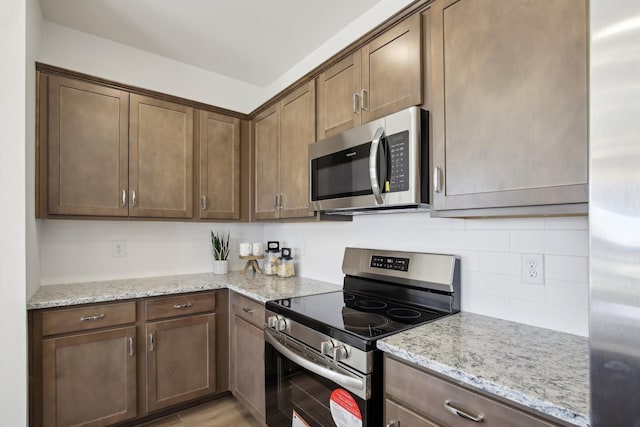 kitchen with light wood-style floors, light stone countertops, decorative backsplash, and stainless steel appliances