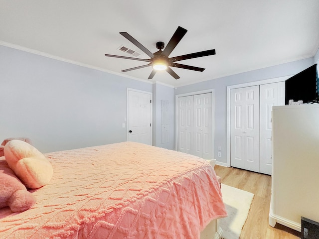 bedroom with visible vents, baseboards, multiple closets, ornamental molding, and light wood-style flooring