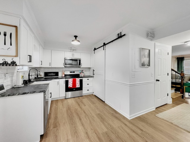 kitchen with a sink, dark countertops, a barn door, light wood-style floors, and appliances with stainless steel finishes