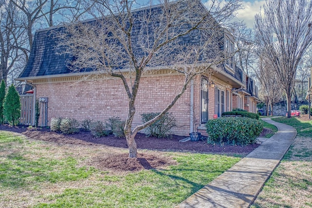 view of side of home with mansard roof, brick siding, a lawn, and a shingled roof