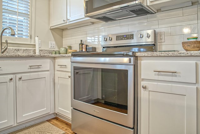 kitchen featuring light stone counters, light wood-style flooring, stainless steel range with electric cooktop, white cabinetry, and backsplash