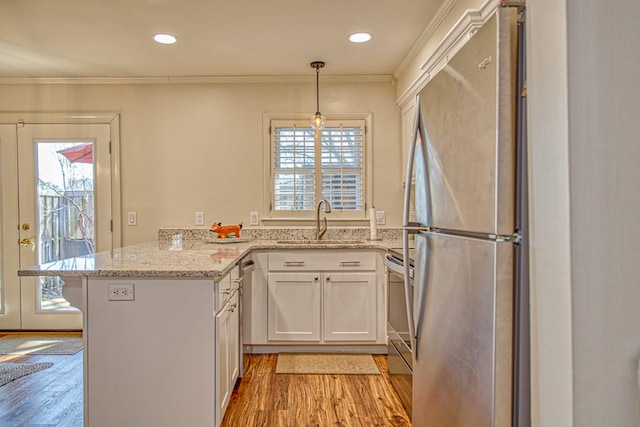 kitchen featuring crown molding, light wood-type flooring, appliances with stainless steel finishes, a peninsula, and a sink