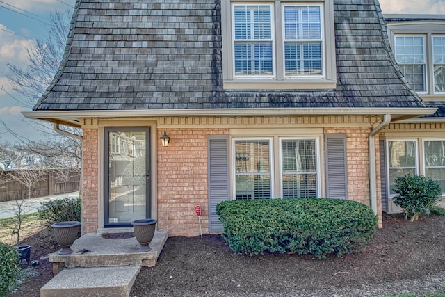 view of exterior entry with fence and brick siding