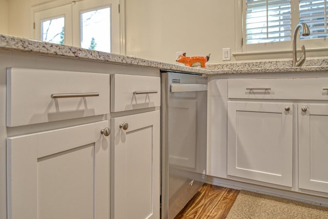 kitchen with light stone counters, stainless steel dishwasher, a sink, and white cabinetry