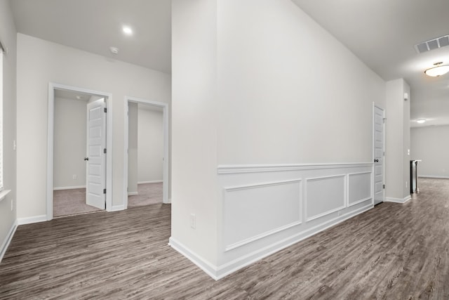 corridor with a decorative wall, wood finished floors, visible vents, and baseboards