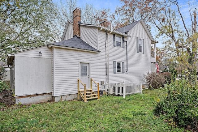 back of house featuring entry steps, a chimney, a yard, and roof with shingles