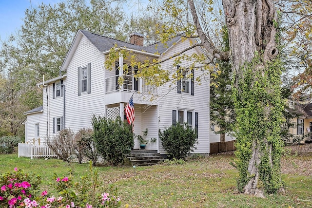 view of front of house with a balcony, a chimney, and a front yard