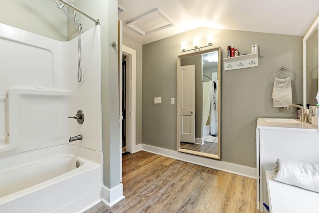 bathroom featuring wood finished floors, baseboards, bathing tub / shower combination, vanity, and vaulted ceiling